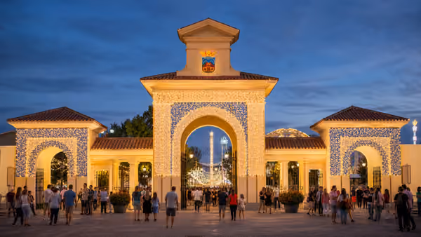 Recreación editorial de la puerta del recinto ferial iluminada al anochecer, con gente entrando bajo los arcos