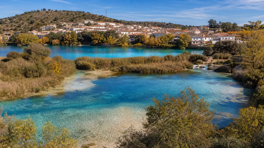Recreación editorial de dos lagunas de agua turquesa con el pueblo de Ruidera en la ladera del fondo