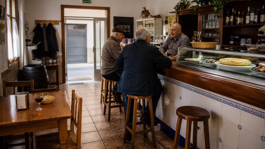 Recreación editorial de tres hombres mayores charlando en la barra de un bar de pueblo, con una tortilla en la vitrina