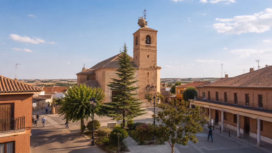 Recreación editorial de una iglesia de ladrillo con torre campanario junto a una plaza con soportales