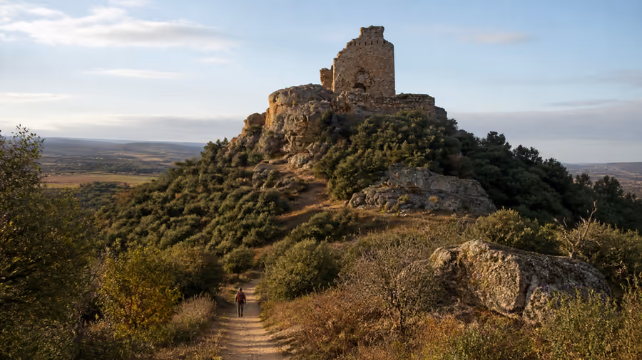 Recreación editorial de un castillo en ruinas sobre un cerro, con un sendero subiendo entre la vegetación