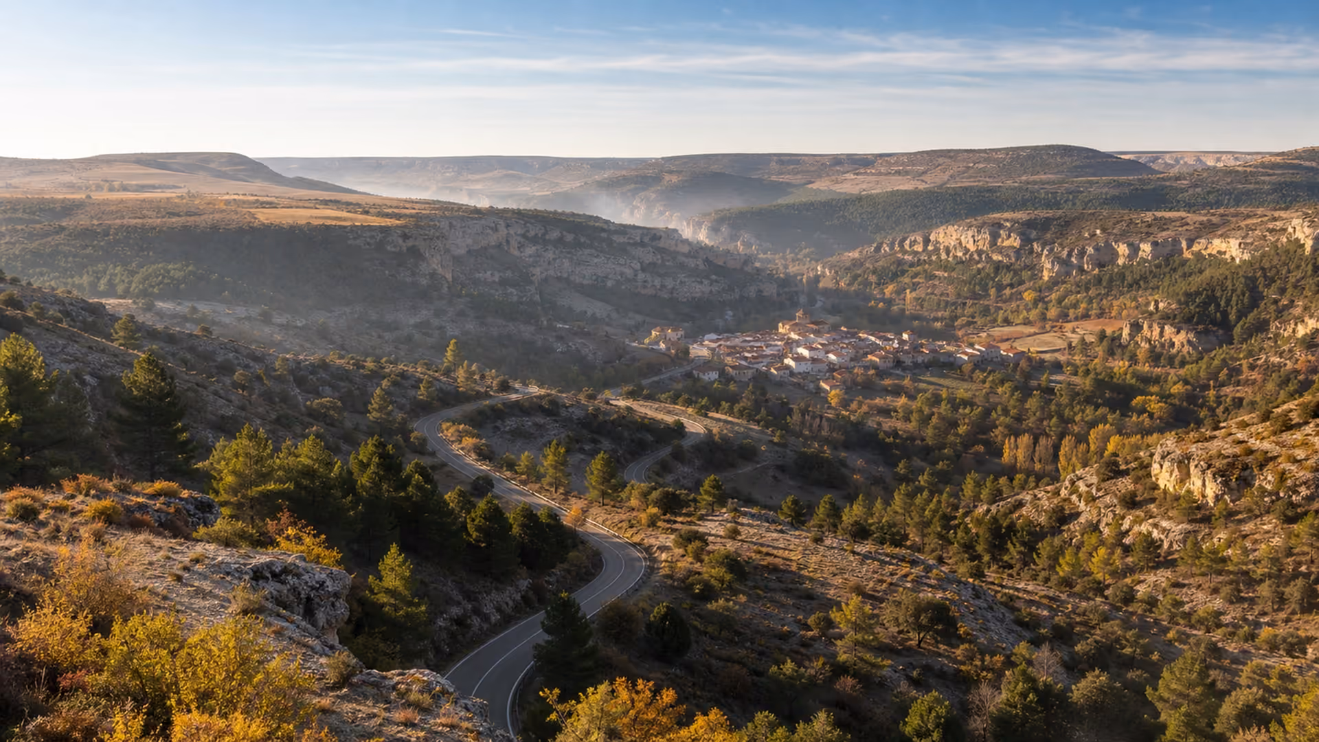 Recreación editorial de una carretera de curvas sobre un valle encajado, con un pueblo pequeño en el fondo