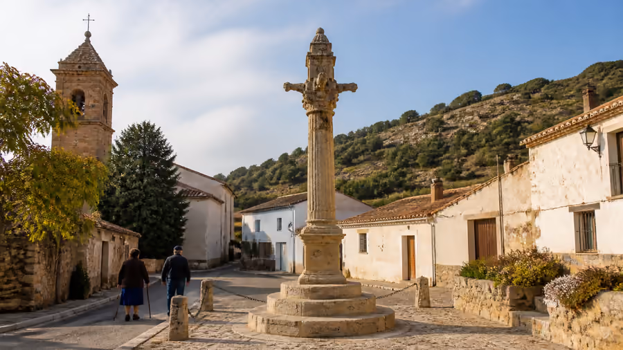 Recreación editorial de un rollo-picota de piedra en el centro de una plaza, con dos vecinos caminando y la iglesia al fondo