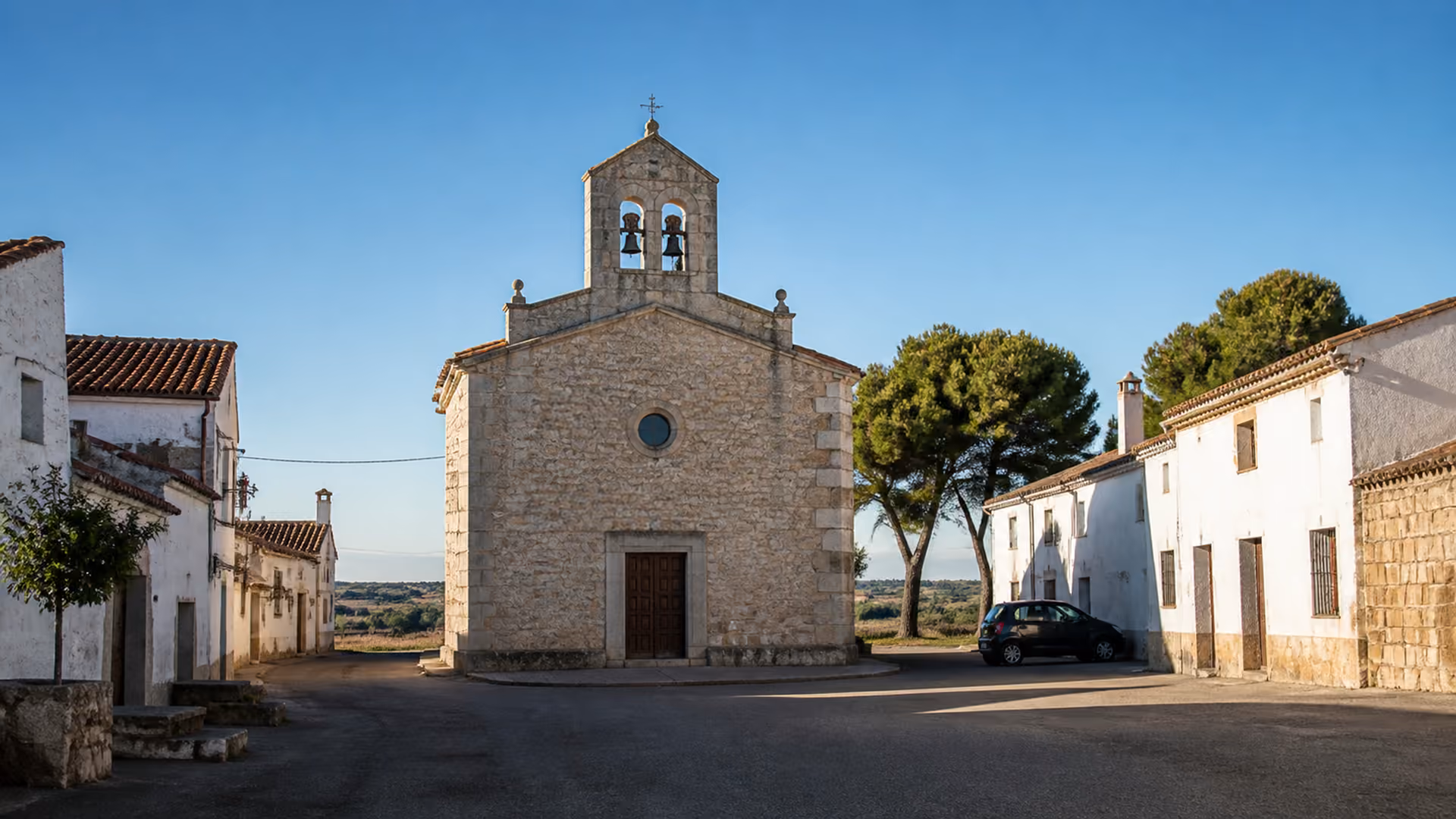 Recreación editorial de una iglesia de piedra con espadaña de dos campanas en una plaza vacía de pueblo