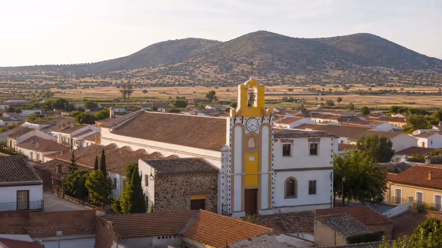 Recreación editorial de una iglesia con torre campanario amarilla y un cerro volcánico del Campo de Calatrava al fondo