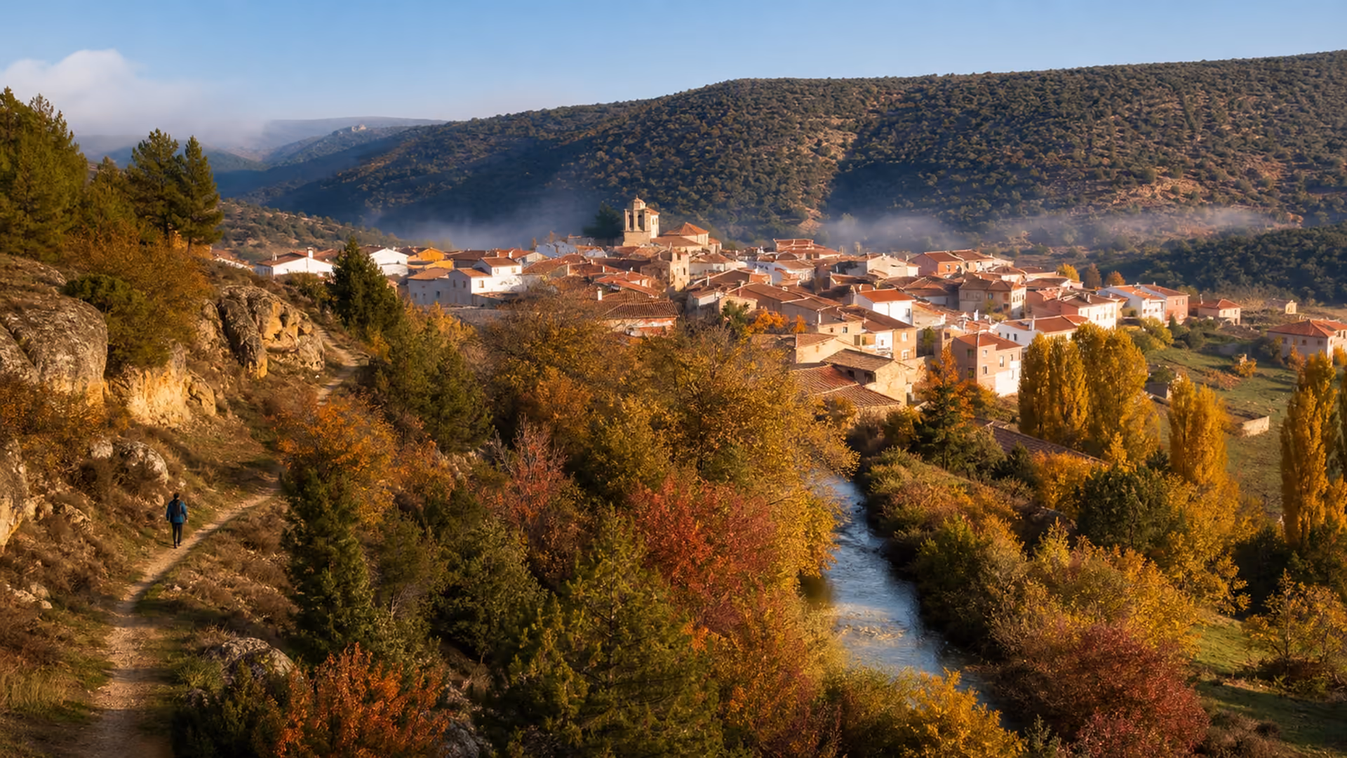 Recreación editorial de un pueblo en un valle con la arboleda del río en colores de otoño y un senderista en primer plano