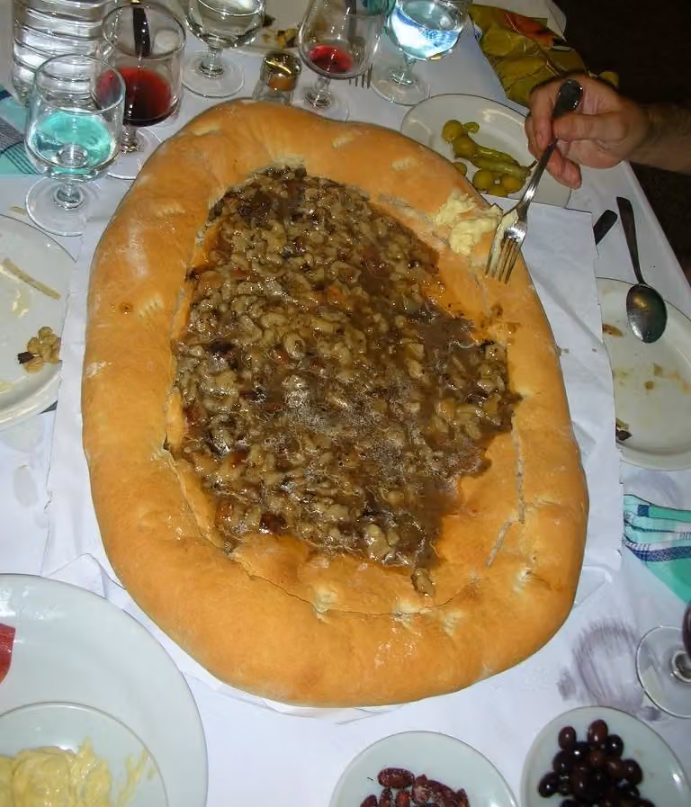 Fotografía de 2009 de gazpachos en Castalla servidos sobre una gran torta ovalada de pan, en una mesa compartida