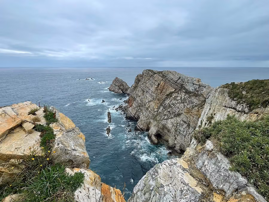 Acantilados, rocas y vegetación de Cabo Peñas frente al Cantábrico bajo un cielo nublado